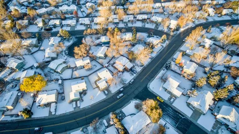 An aerial view of a homes covered in snow in a suburban neighborhood.